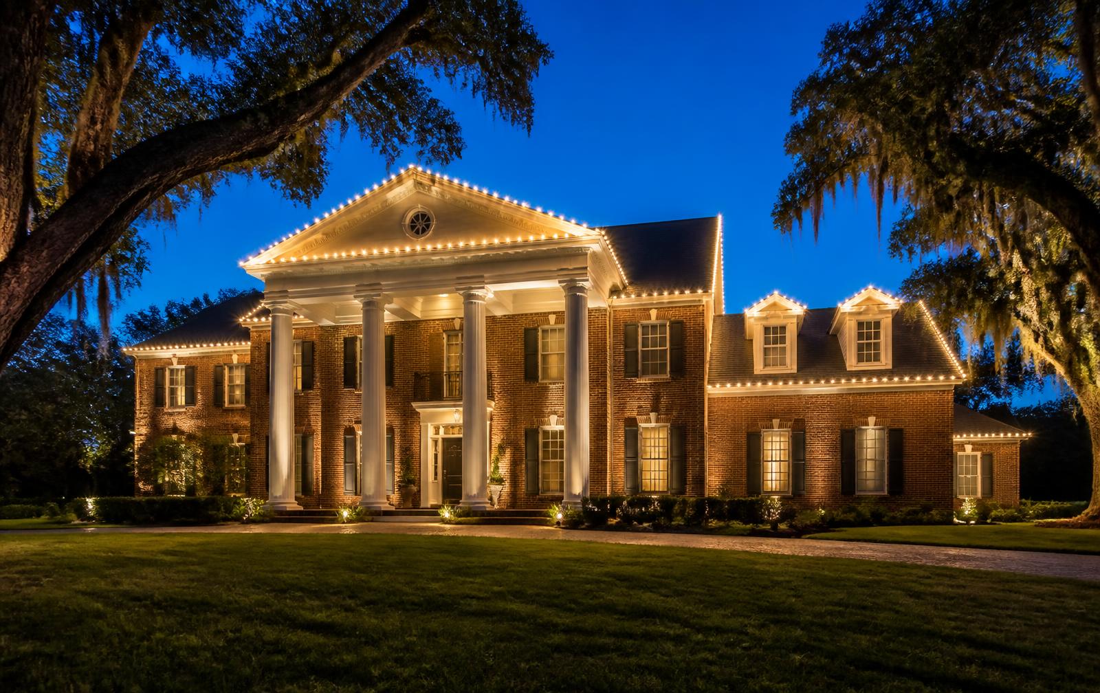 Southern home with warm white Christmas lights outlining the roofline at dusk